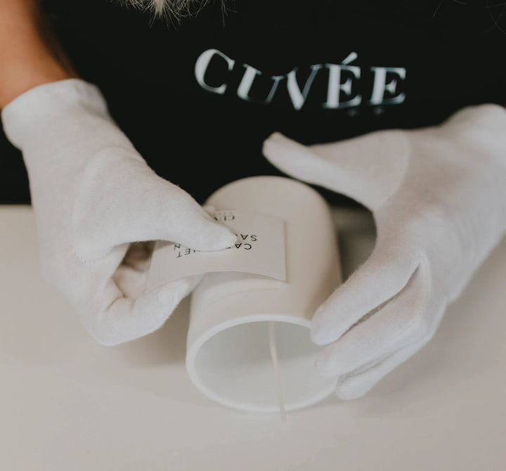 Behutsame Handarbeit beim Anbringen der edlen Etiketten der deutschen Luxusduftkerzen von CUVÉE CANDLES in weißen Baumwollhandschuhen.