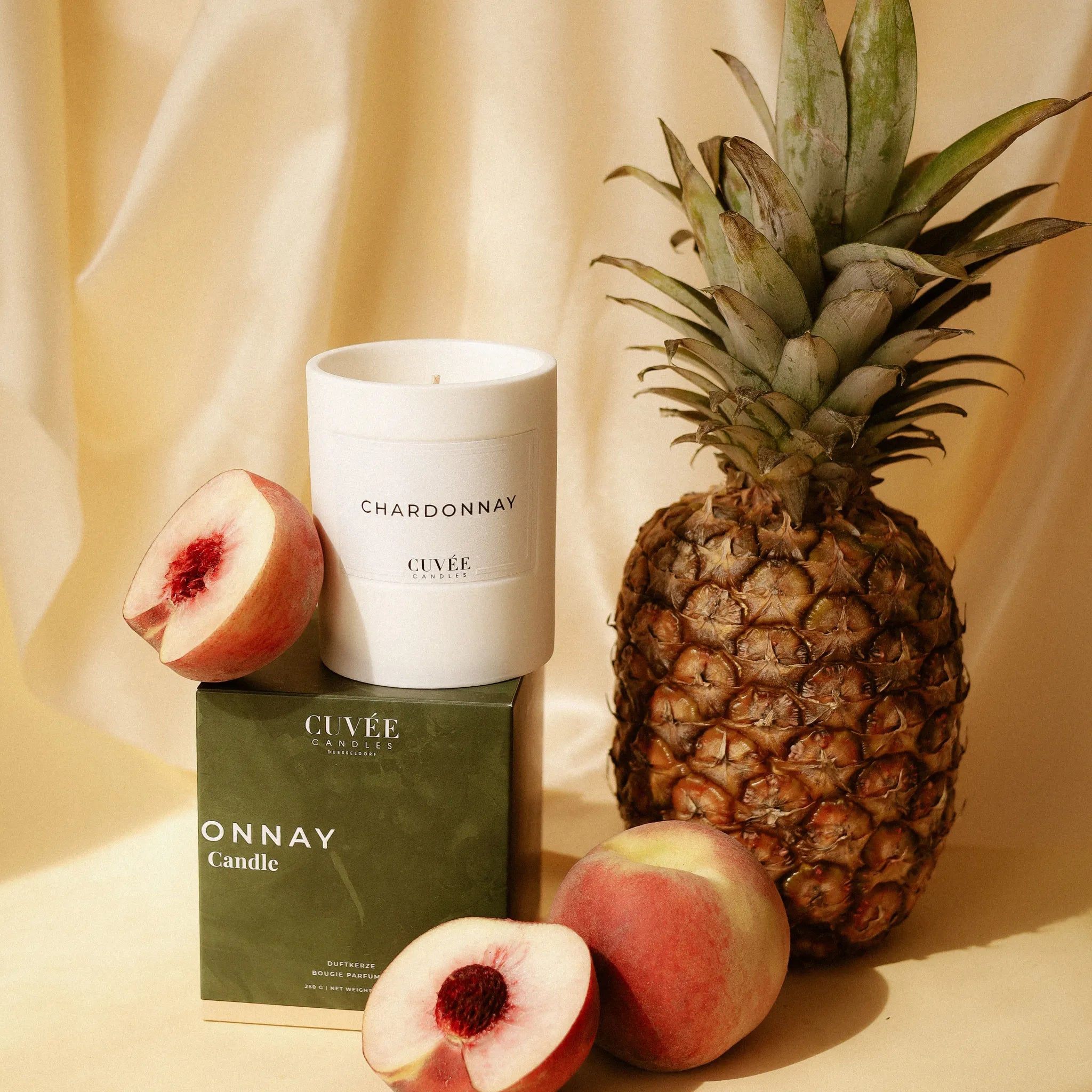CUVÉE Duftkerze Chardonnay zwischen Ananas und Pfirsichen vor warmem, hellem Hintergrund
