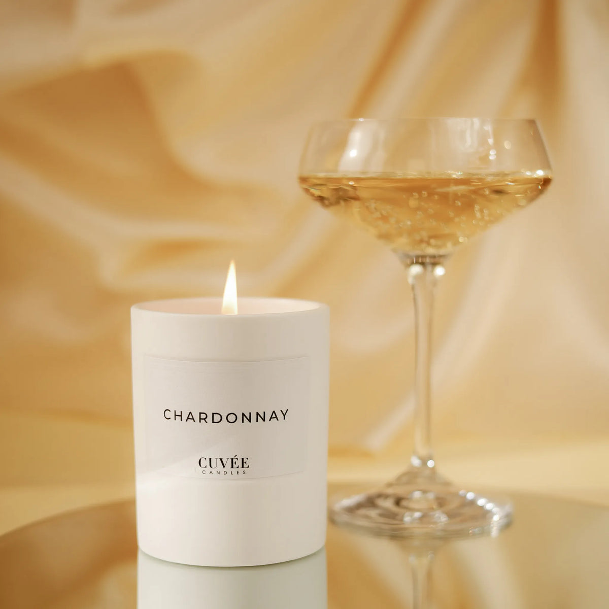 CUVÉE Duftkerze Chardonnay neben einer gefüllten Champagnerschale vor beigem Hintergrund
