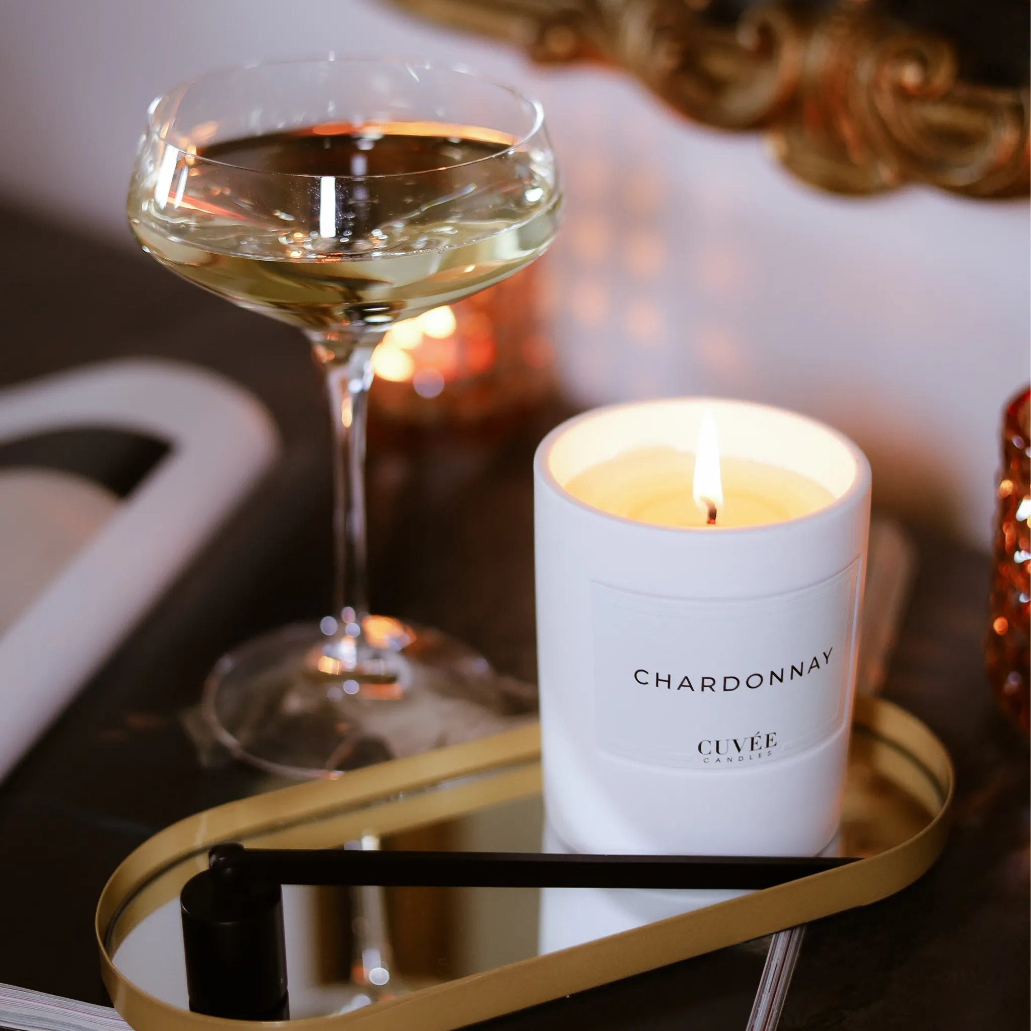 Brennende CUVÉE Duftkerze Chardonnay auf einem goldenen Tablett neben einem Glas Champagner