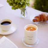 Brennende CUVÉE Duftkerze Riesling auf einem Frühstückstisch mit Kaffee, Croissant und Blumen