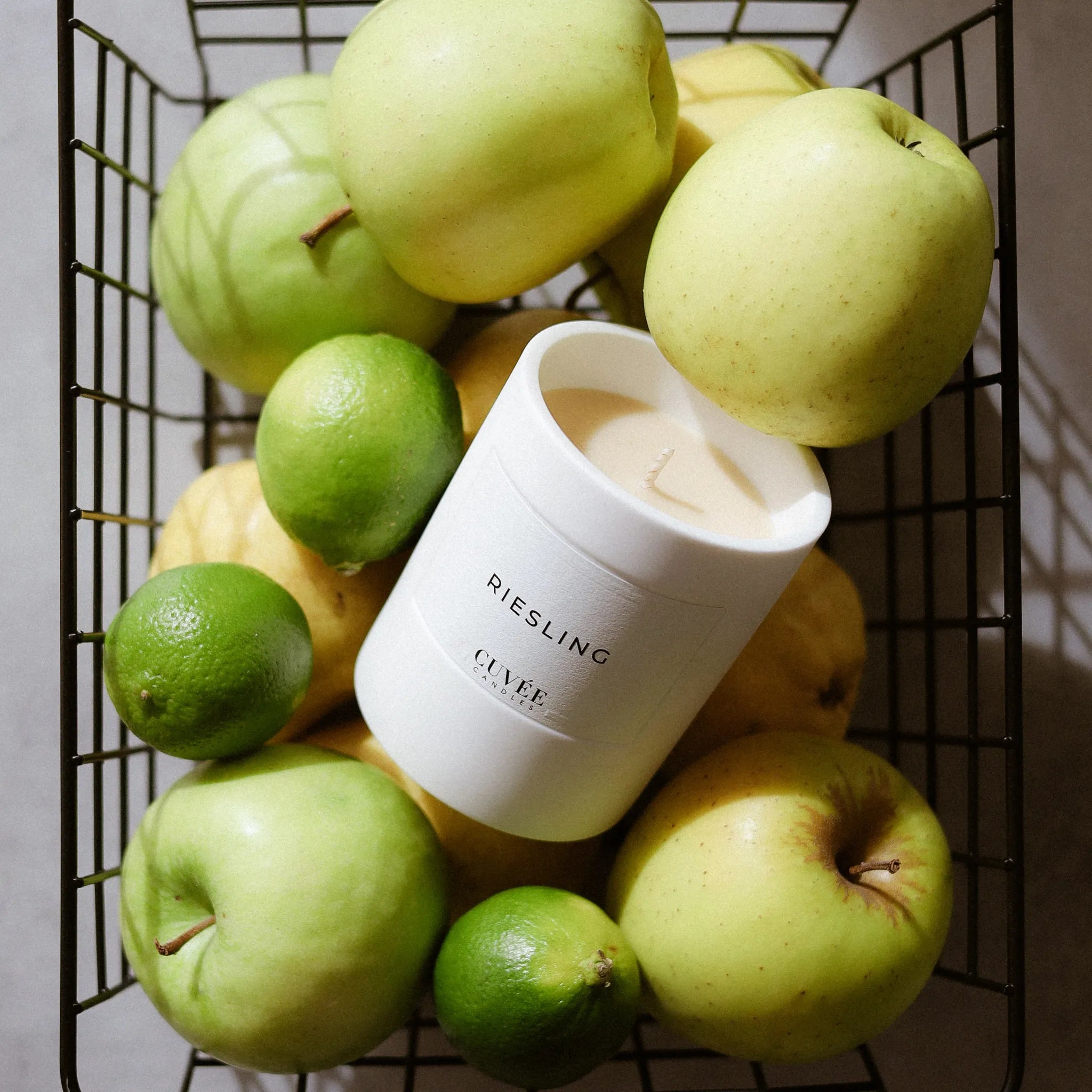 CUVÉE Duftkerze Riesling in einem Drahtkorb voller grüner Äpfel