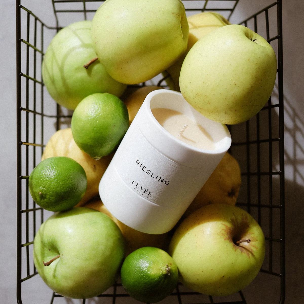 CUVÉE Duftkerze Riesling in einem Drahtkorb voller grüner Äpfel