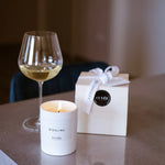 CUVÉE Duftkerze Riesling neben einem Glas Weißwein und einer Geschenkbox mit Schleife