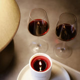 Brennende CUVÉE Duftkerze Cabernet Sauvignon mit bordeauxrotem Wachs vor zwei Gläsern Rotwein