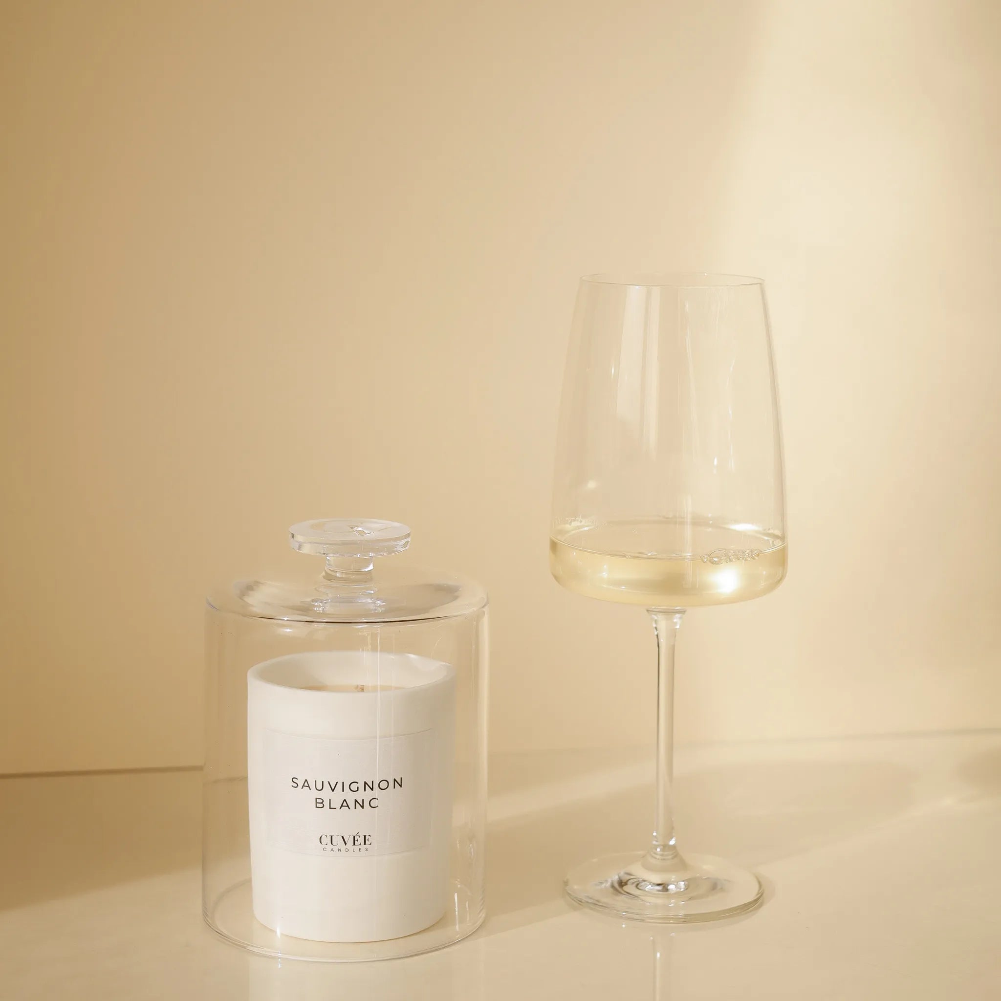CUVÉE Duftkerze Sauvignon Blanc unter einer Duftglocke aus Glas neben einem Glas Weißwein