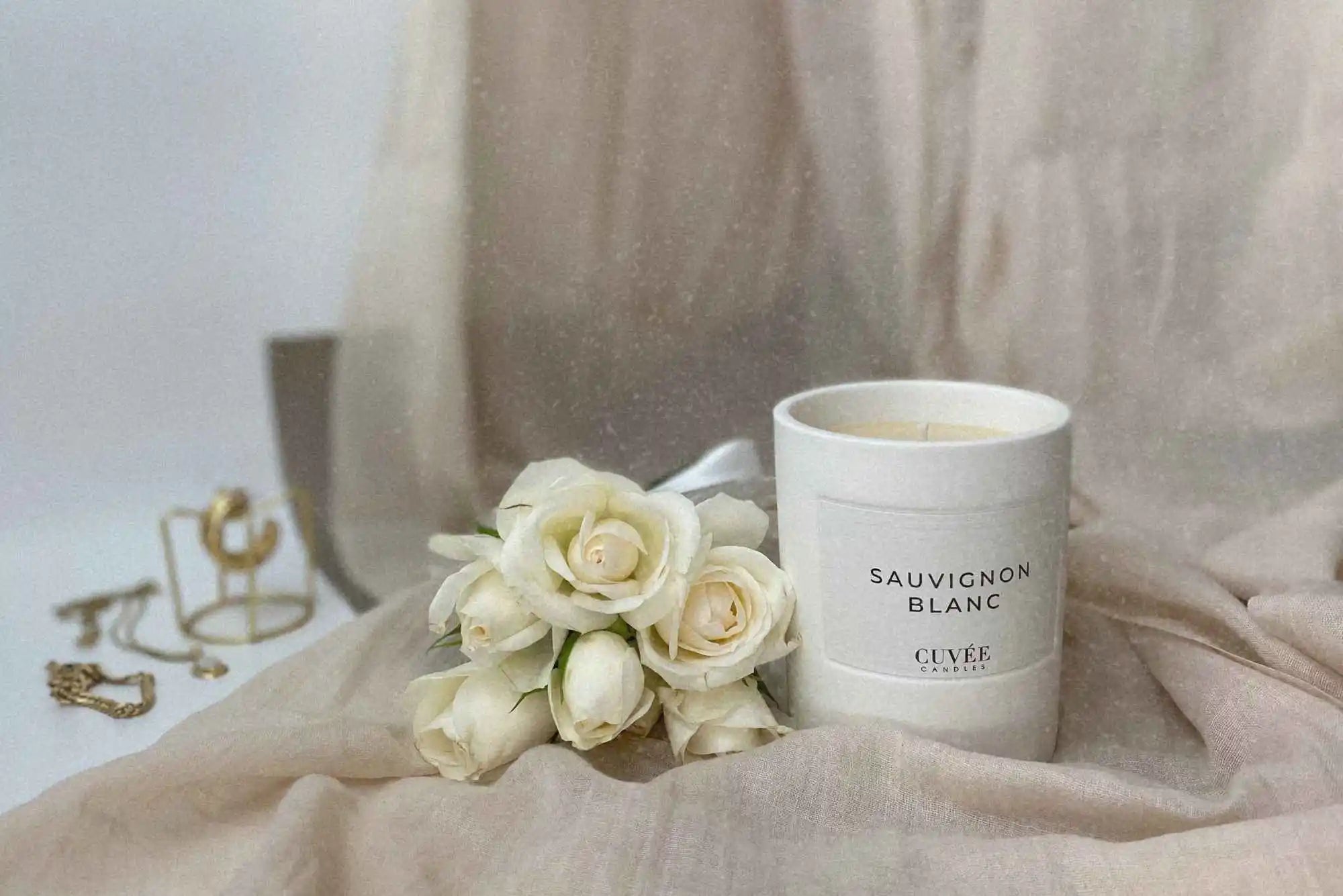 Edle weiße Rosen und Echtgoldschmuck, Ehering und Verlobungsring neben luxuriöser, weißer Sauvignon Blanc Duftkerze von CUVÉE CANDLES als einzigartige Erinnerung an den Hochzeitstag.