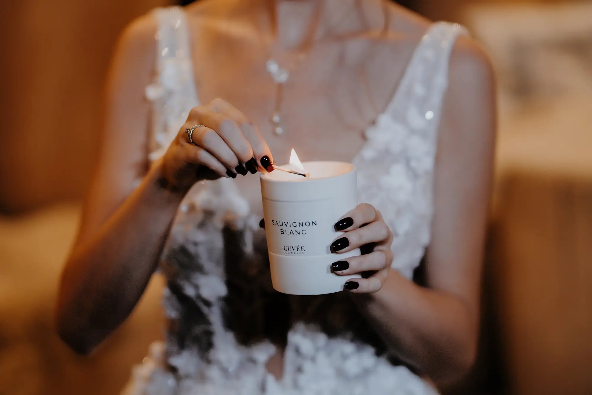 Braut im Hochzeitskleid beim Anzünden der luxuriösen Hochzeitsduftkerze CUVÉE CANDLES Sauvignon Blanc.