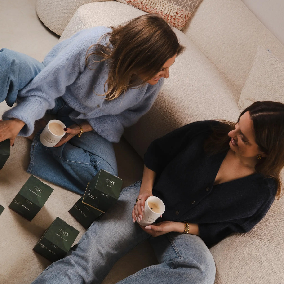Die beiden Gründerinnen Miriam und Katharina im Gespräch auf dem Sofa, beide mit CUVÉE CANDLES Duftkerzen in der Hand