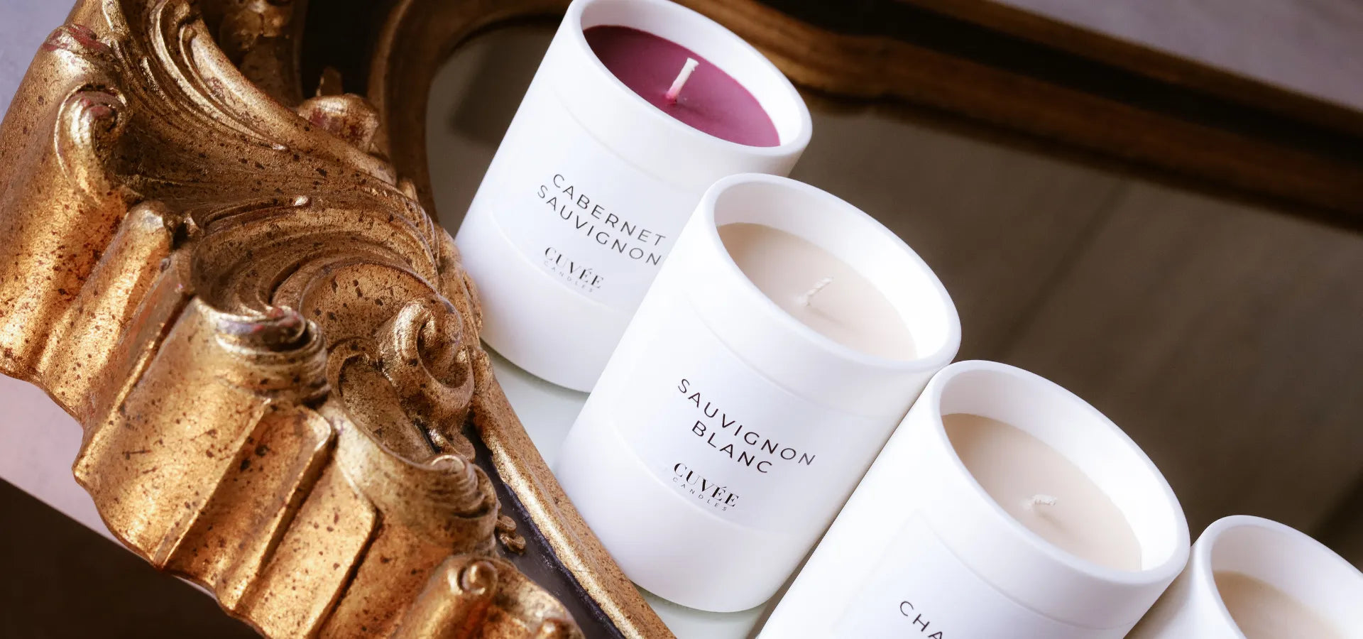 Mehrere Duftkerzen von CUVÉE CANDLES stehen auf einem Spiegelrahmen.